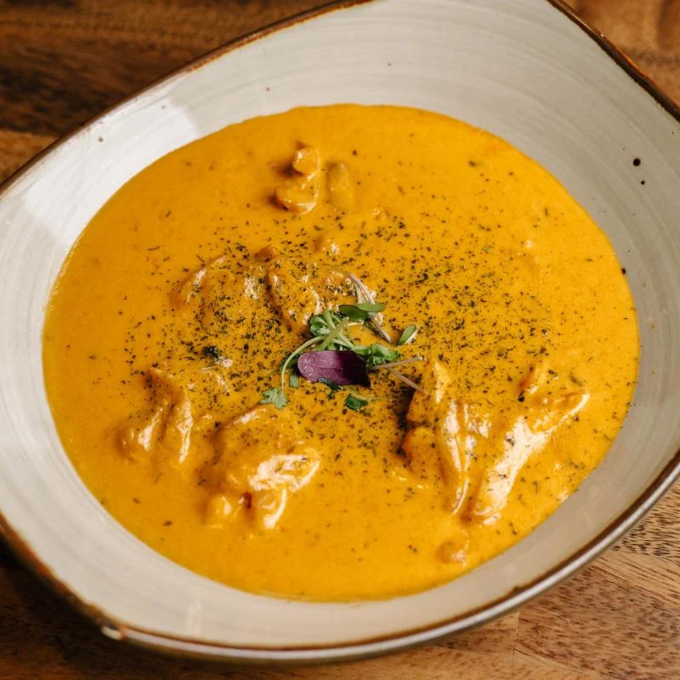 Creamy orange curry with shrimp, herbs, and purple edible flower garnish served in a white bowl on a wooden table.