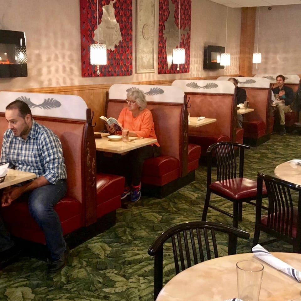 Warmly lit restaurant dining room with red booths, patterned carpet, wall art, and several diners enjoying meals.