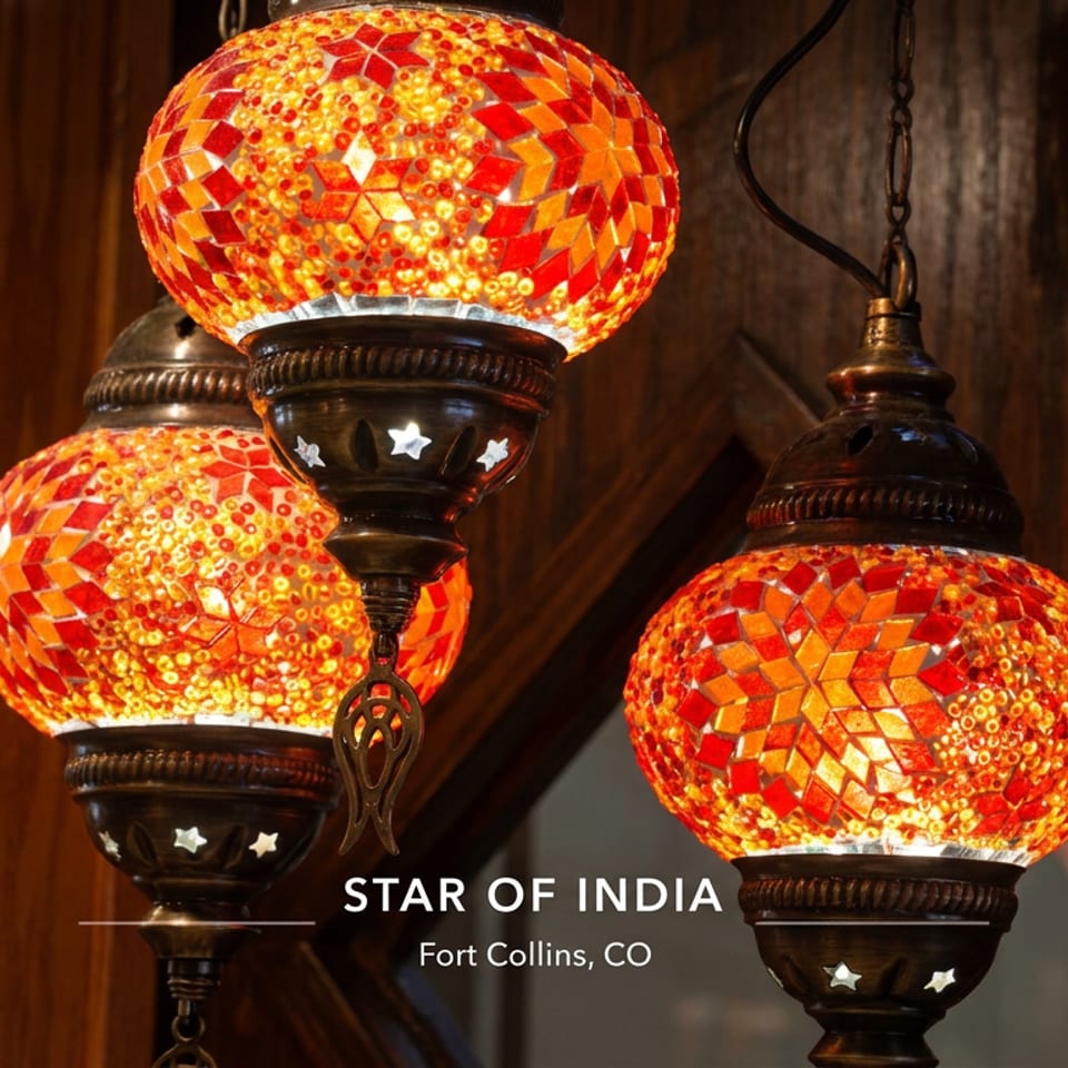 Three glowing red-and-gold mosaic pendant lamps hang against dark wood at Star of India restaurant in Fort Collins, Colorado.