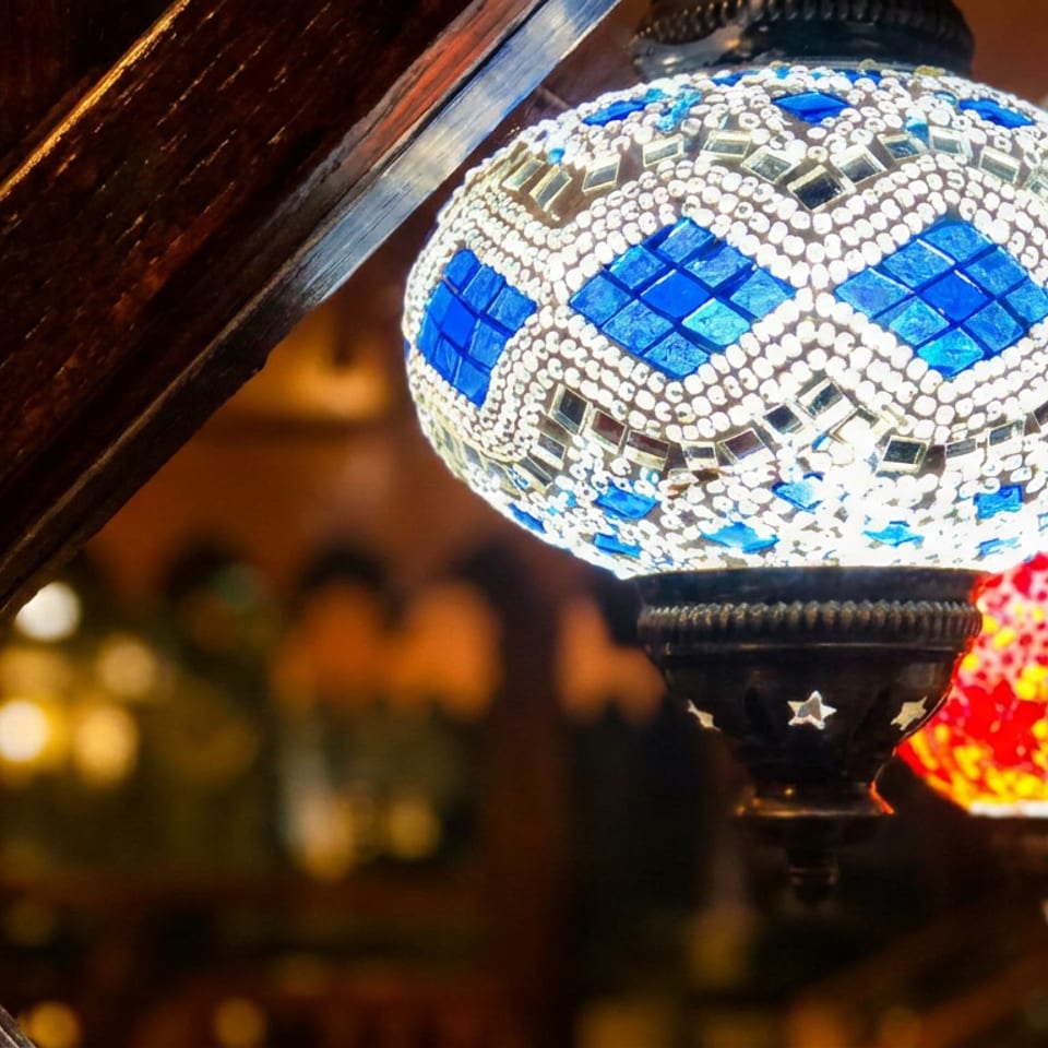 Ornate blue-and-white mosaic lamp glows beside red and silver patterned lamps in a warmly lit restaurant interior.