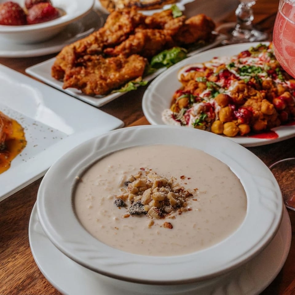Assorted restaurant dishes, including creamy soup, sauced gnocchi, fried chicken, chickpeas, dessert, and a pink cocktail on a wooden table.