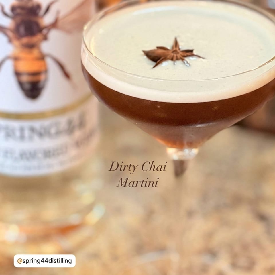 Dirty Chai Martini with creamy foam and star anise garnish in a coupe glass, beside a bottle on a wooden bar.
