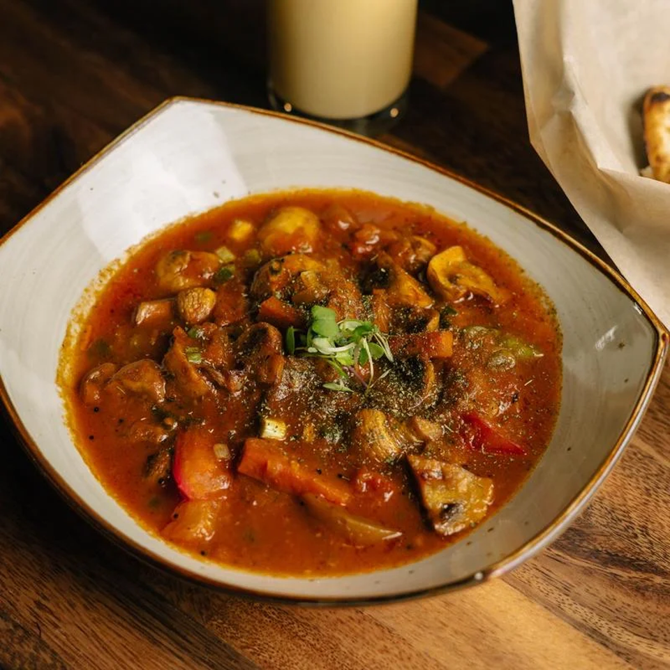 Bowl of hearty tomato-based mushroom stew garnished with fresh cilantro on a rustic wooden table.