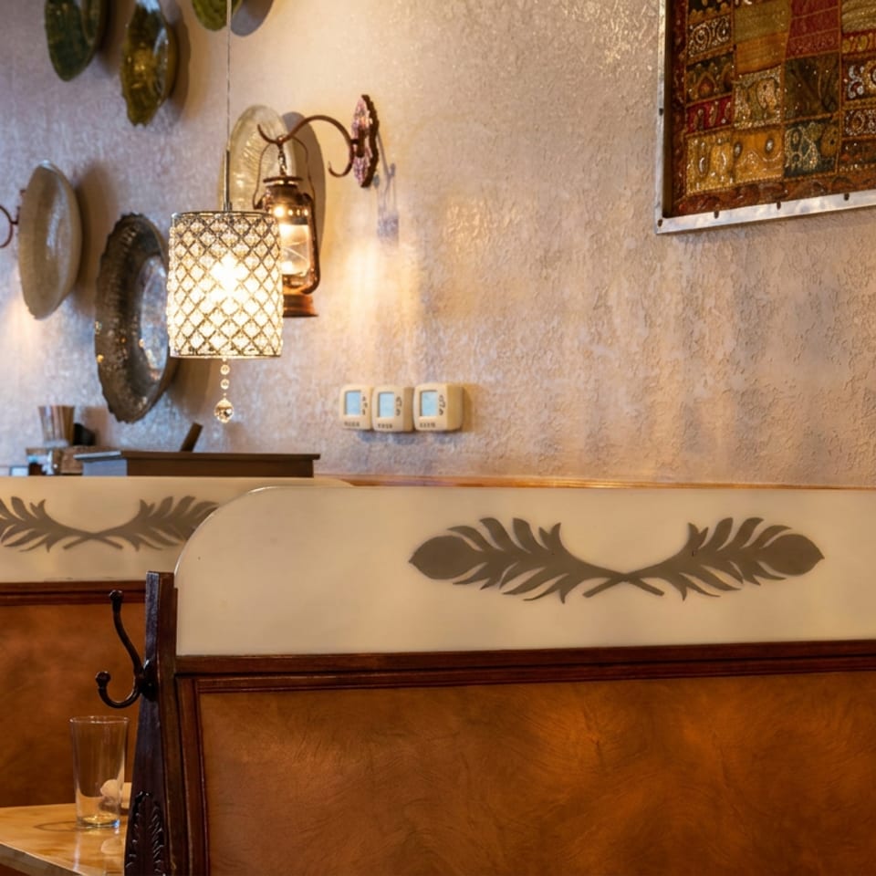 Warmly lit restaurant dining area with wooden booths, cream backs, decorative leaf motifs, patterned wall lamps, and cultural wall art.