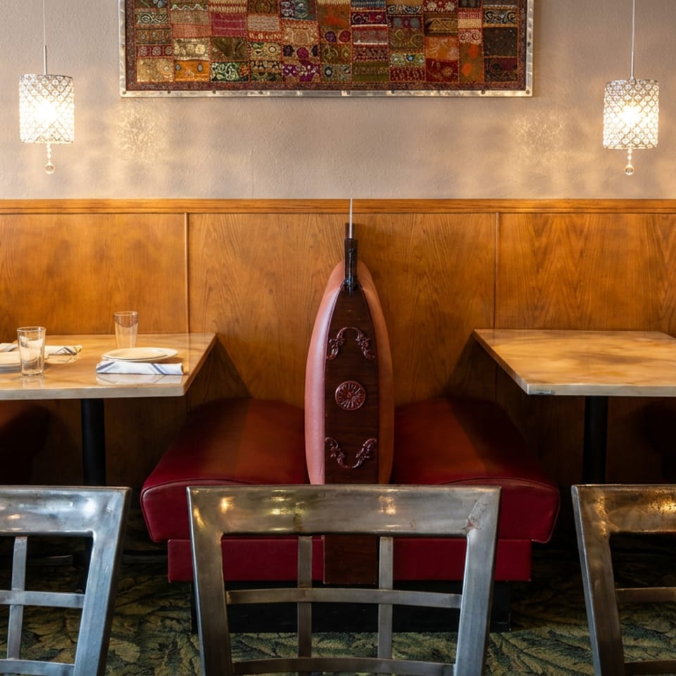 Warmly lit restaurant dining area with red leather booths, wooden tables, metal chairs, patterned artwork, and pendant lamps.